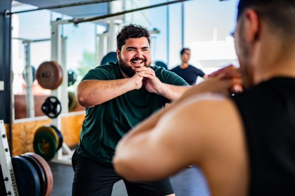 Mid adult man doing squats with personal trainer at gym