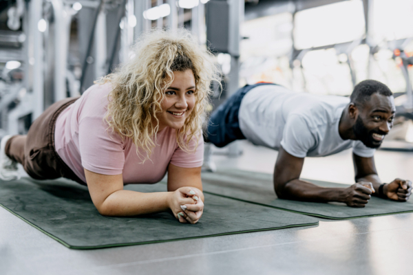 Two friends engage in a planking workout at the gym, exchanging smiles